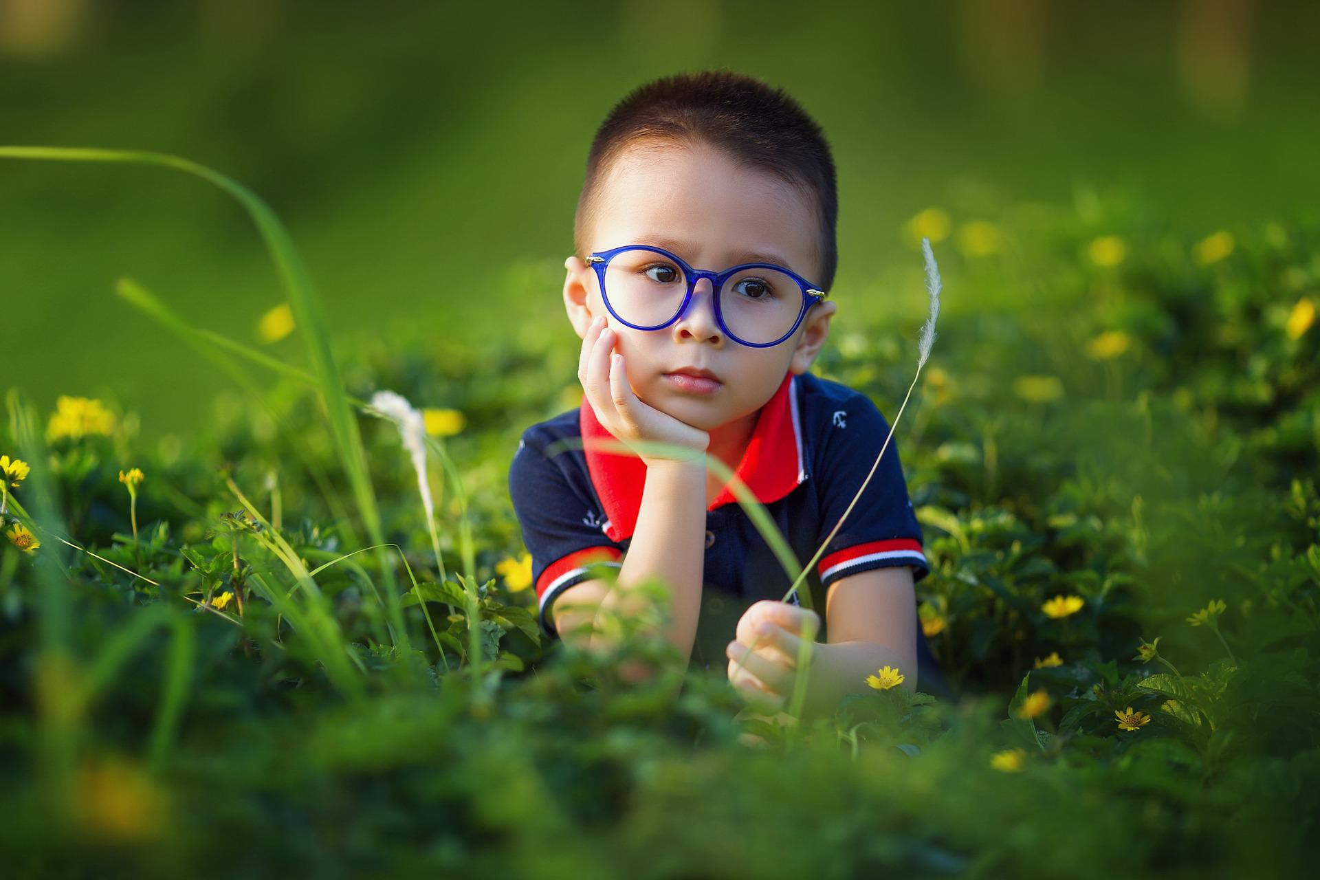 nachdenklicher kleiner Junge mit Brille auf der Wiesse sitzend