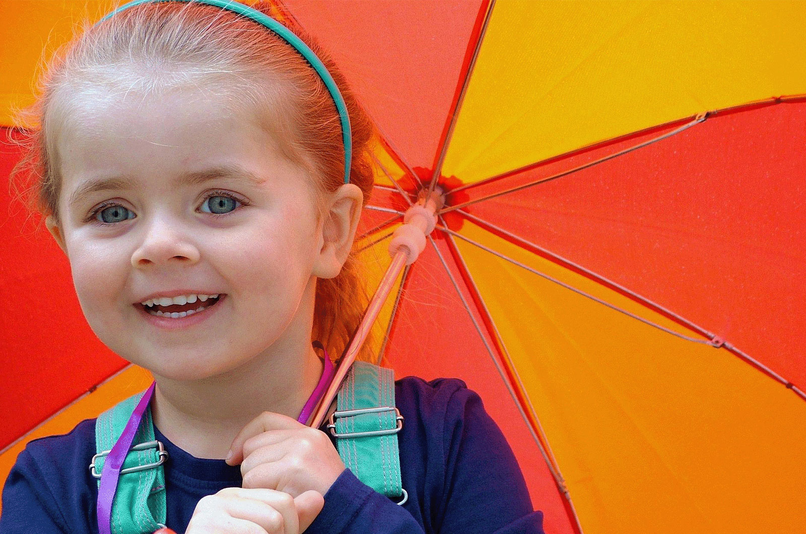 ein lachendes kleines Mädchen mit orange, gelben Sonnenschirm in der Hand
