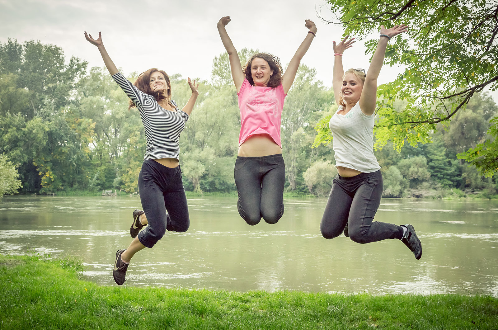 3 junge Frauen an einem Waldsee, in Sportbkleidung, springen hoch in die Luft