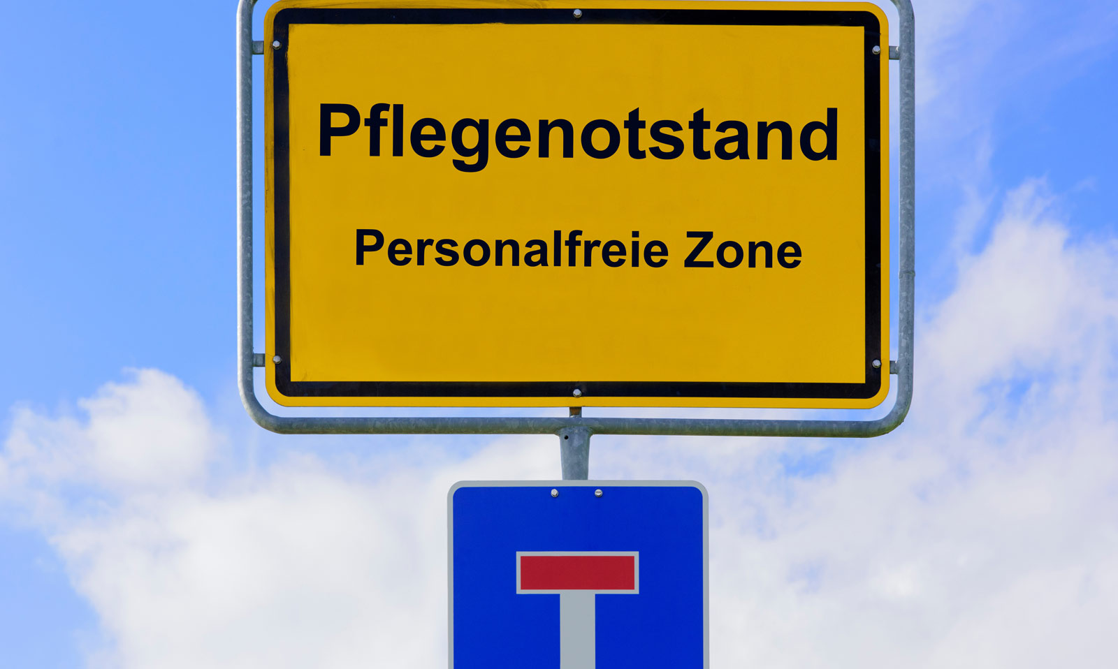 Ein Ortsschild mit der Aufschrift "Pflegenotstand Personalfreie Zone" dadrunter ein Verkehrsschild, welches eine Sackgasse anzeigt