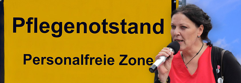 Ein Ortsschild mit der Aufschrift "Pflegenotstand Personalfreie Zone", davor Claudia Lenden