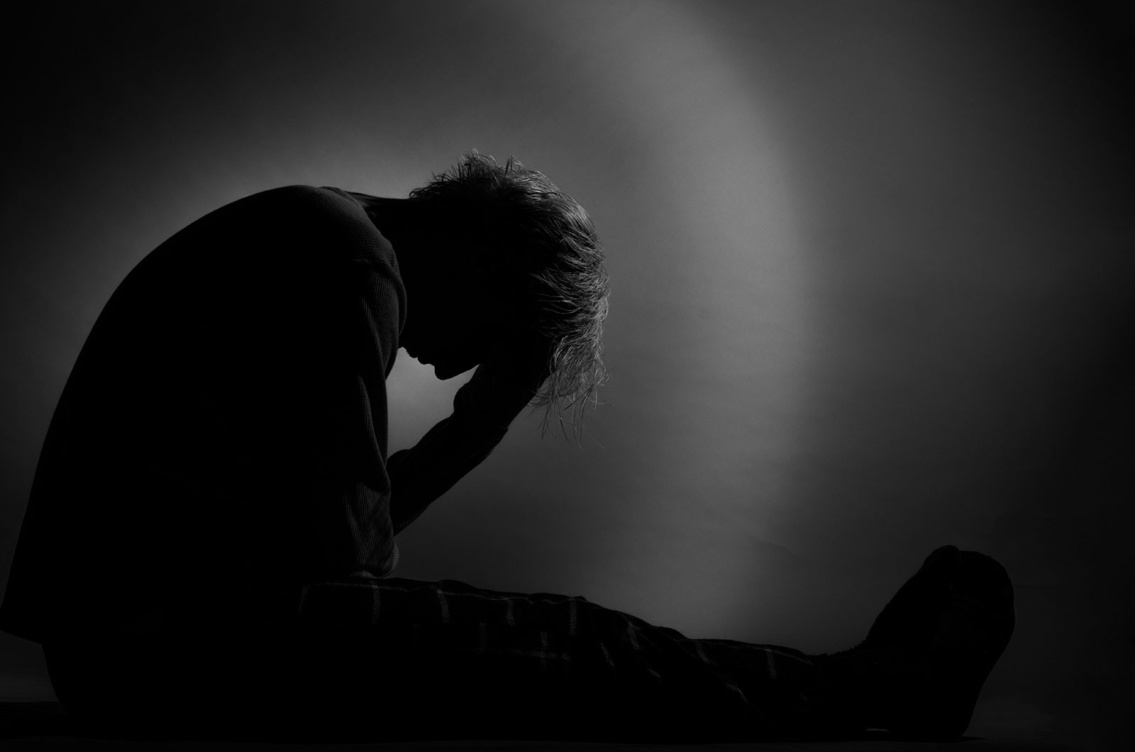 Silhouette eines einsamen Jungen Silhouette eines einsamen Jungen, der seinen Kopf nach vorn neigt und mit beiden Händen hält