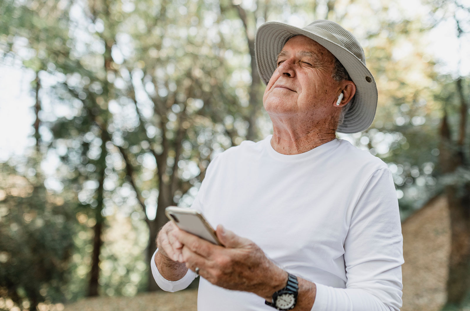 moderner Opa genießt sein digitales Hörbuch in freier Natur mit einem Smartphone