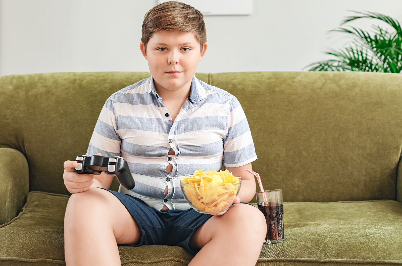 Übergewichtiger Junge sitzt auf der Couch mit Chips und Cola spielt Videospiele