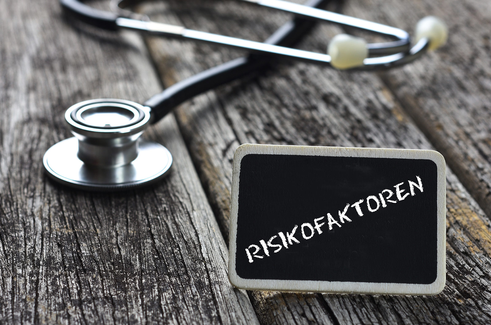 Risikofaktoren Wort RISKIKOFAKTOREN mit Kreide auf Tafel geschrieben, Stethoskop liegt daneben