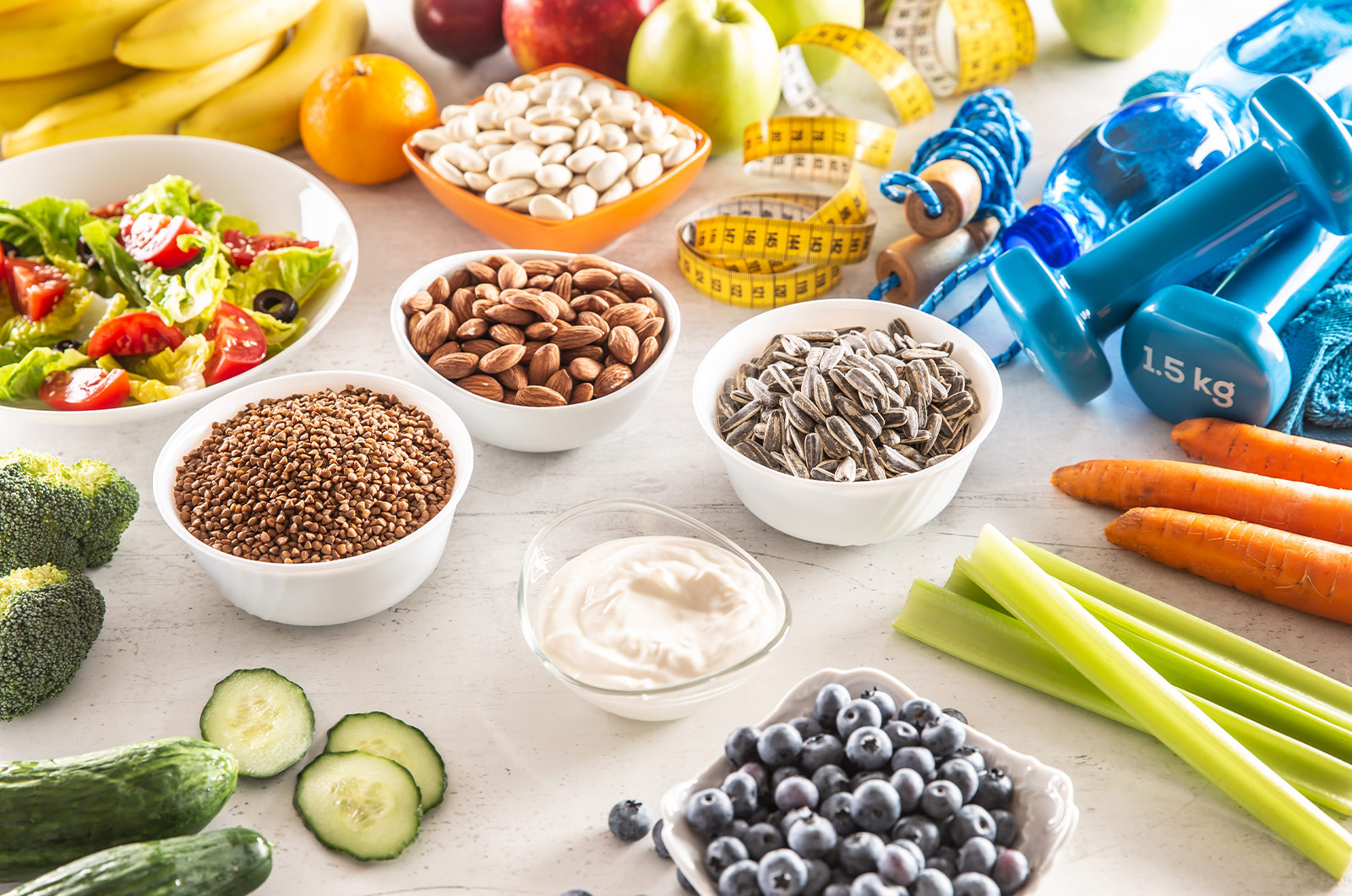 Auswahl an gesunden Lebensmitteln, Gemüse, Obst, Mandeln, Salat, Trainingsgeräten und Maßband