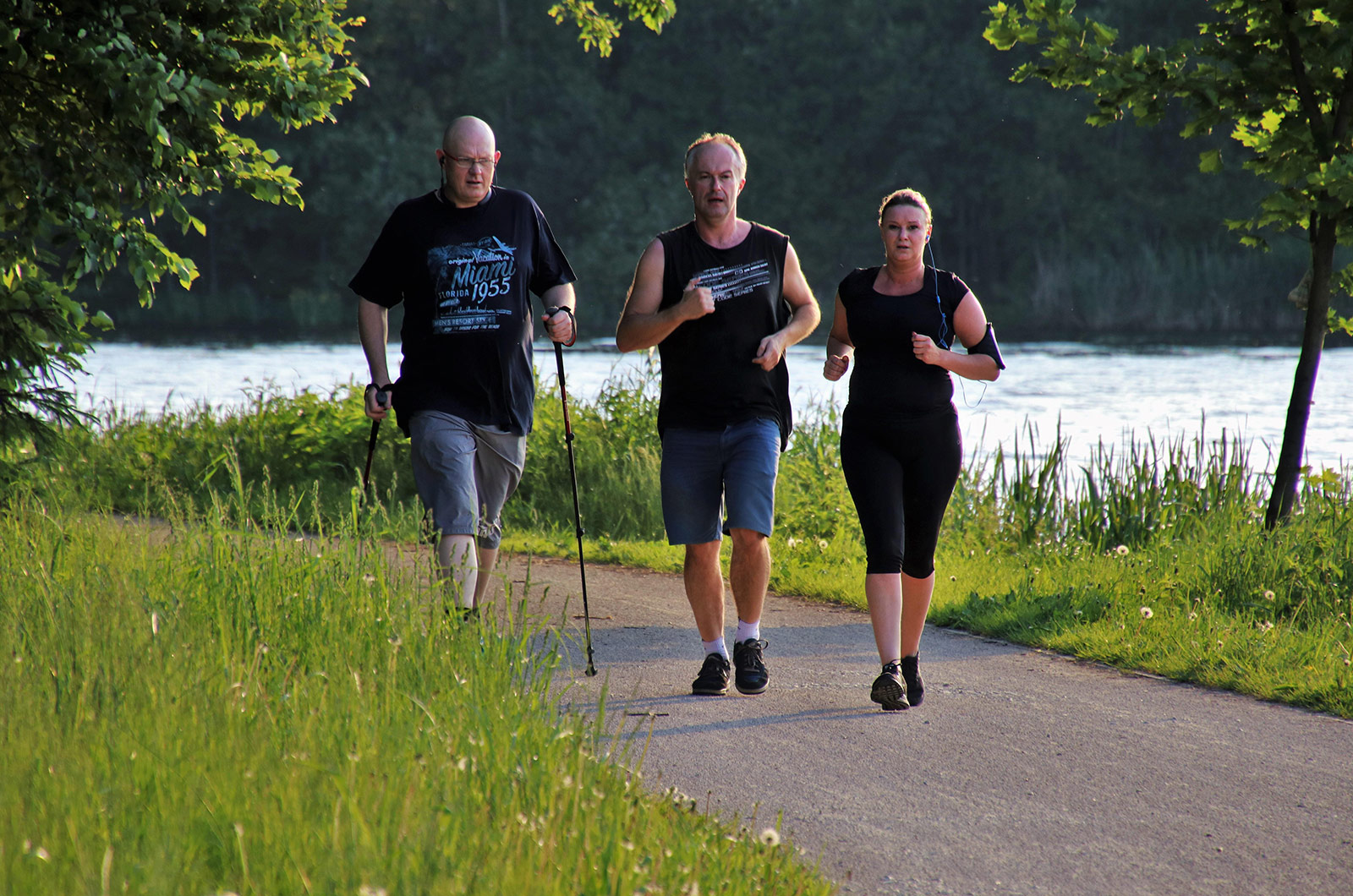 Gruppe beim Walking, eine Frau und zwei Männer beim Walking in einem Park um einen See