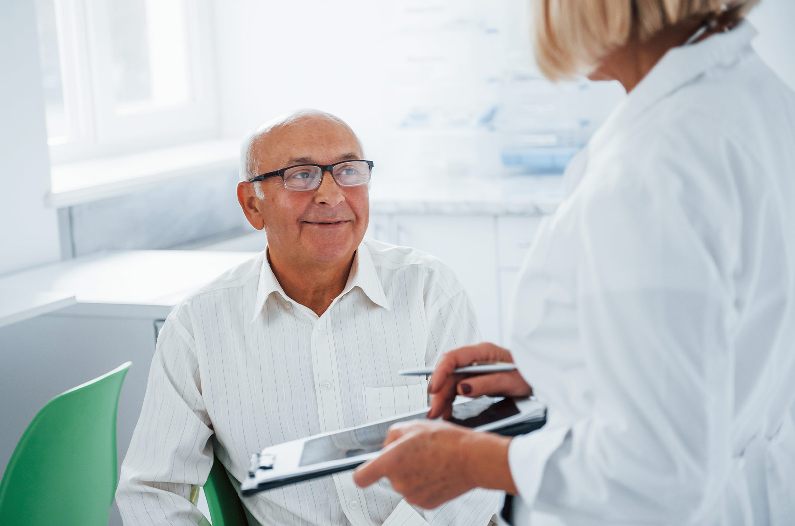 älterer Mann wird in einer Klinik von einer freundlichen Ärztin konsultiert und führt ein beratendes Gespräch