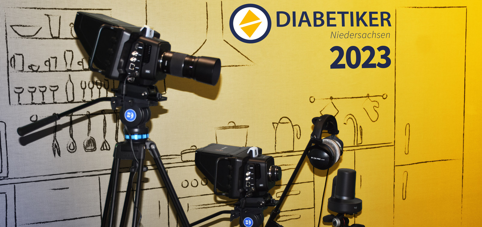Professionelle Kameras vor einer Rückwand mit dem neuen Logo der Diabetiker Niedersachsen. Darunter steht "2023"