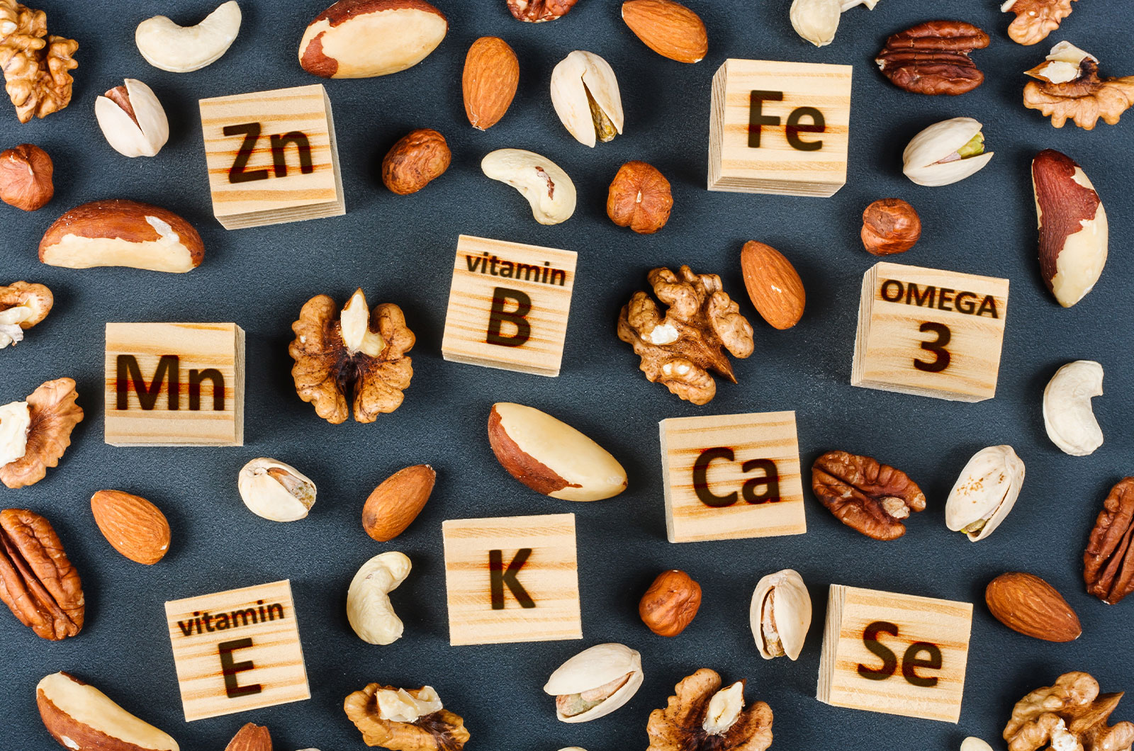 Kleine Holzbausteine mit Buchstaben von verschiedenen Arten an Vitaminen und Mineralstoffen mit verschiedenen Sorten Nüsse