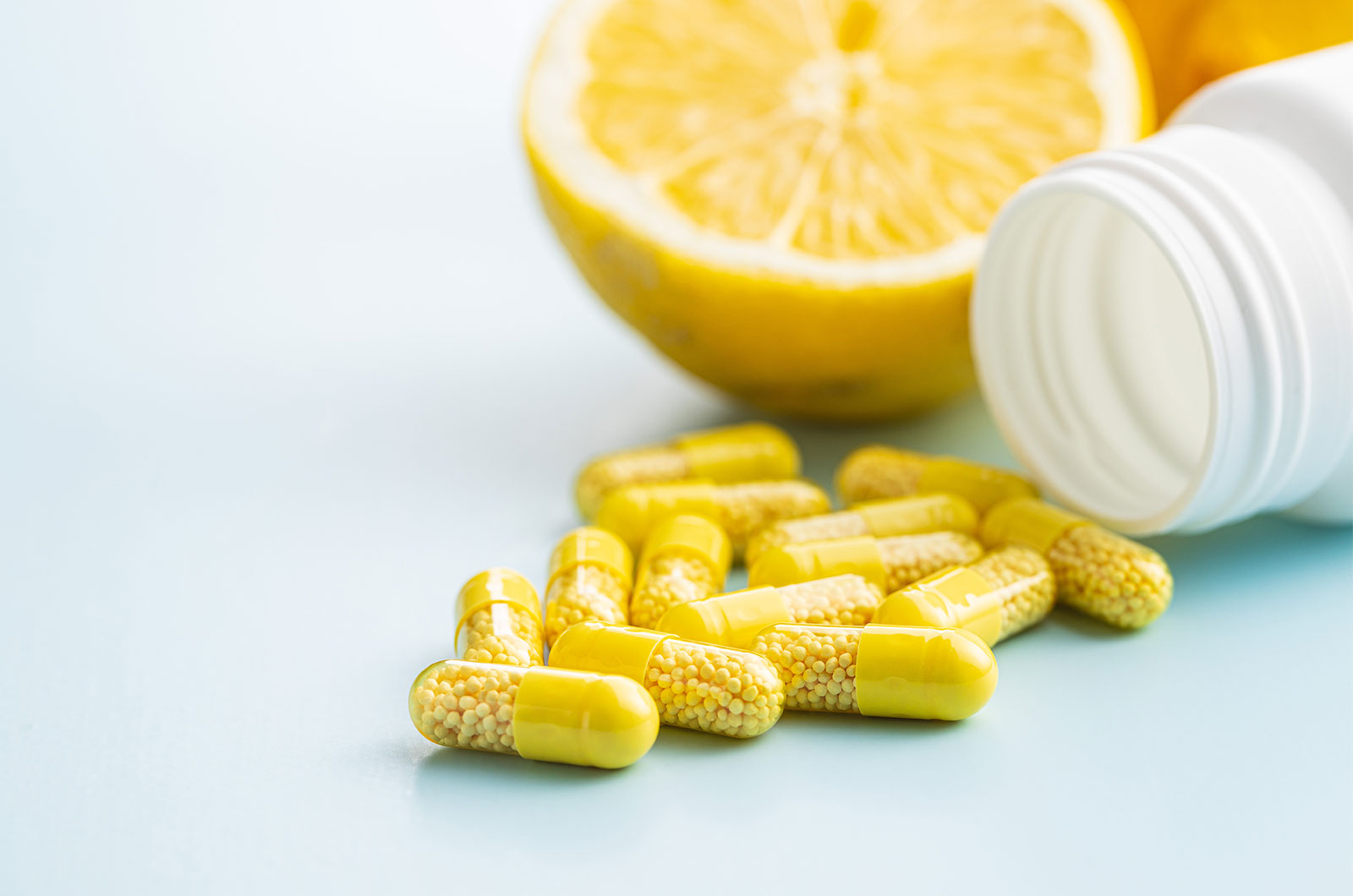 Vitamin C Kapseln mit einer Pillendose und eine frisch aufgeschnittene Zitrone
