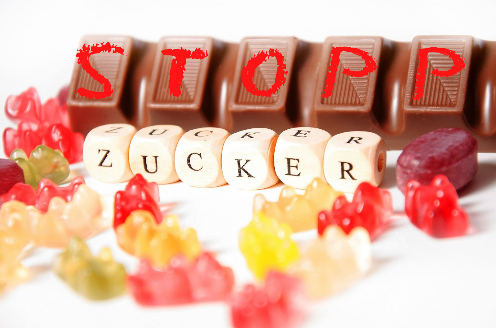 Auf einem Riegel Schokolade steht "Stopp", darunter bilden Buchstabenwüfel das Wort "Zucker"