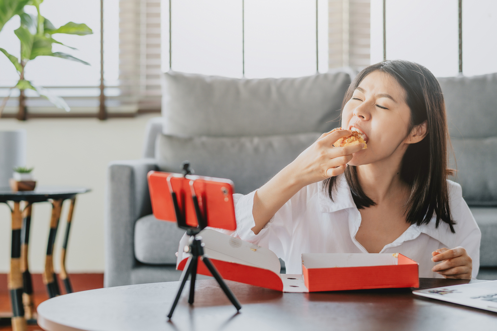 Eine junge Frau ist ein fettiges Stück Pizza und filmt sich dabei mit dem Handy.