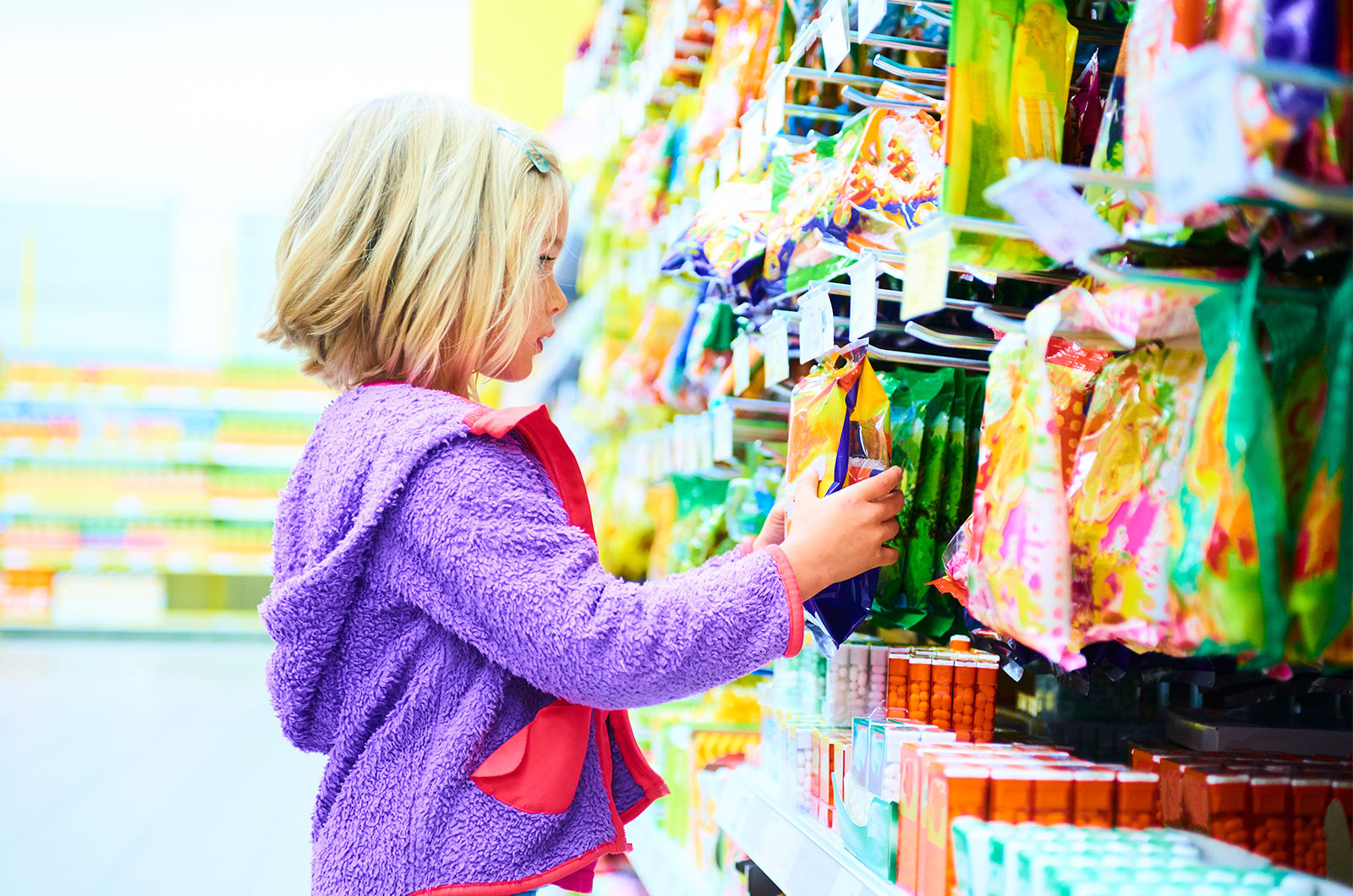 Kind im Supermarkt vor einer Wand mit Süßigkeiten