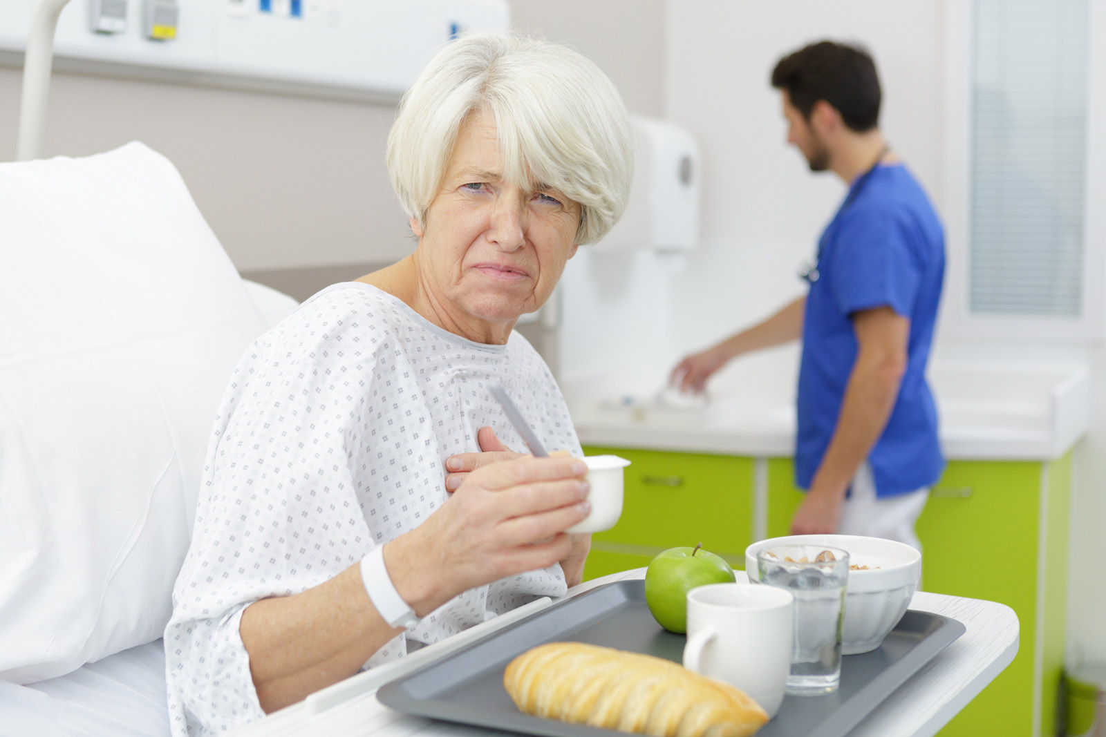 EIne ältere Dame sitzt im Krankenbett vor ihrem Menü und guckt verbittert