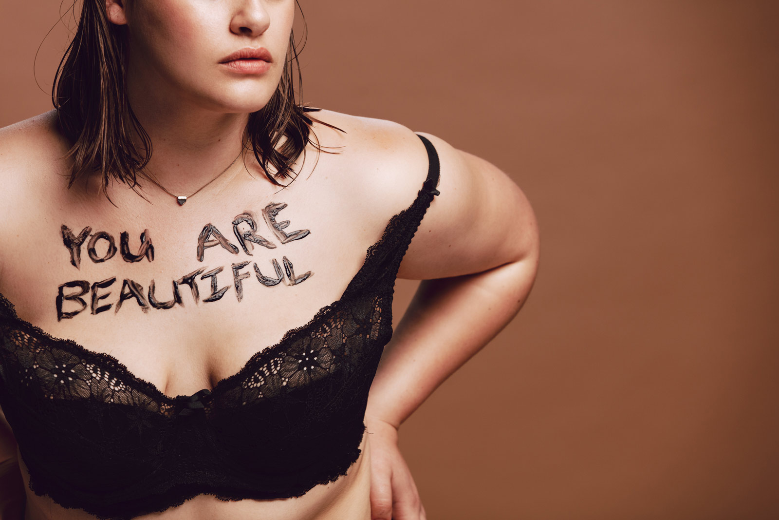 Es ist der leicht bekleidete Oberkörper einer Frau mit Adipositas zu sehen, auf der Brust steht in brauner Farbe: "You are beautiful"