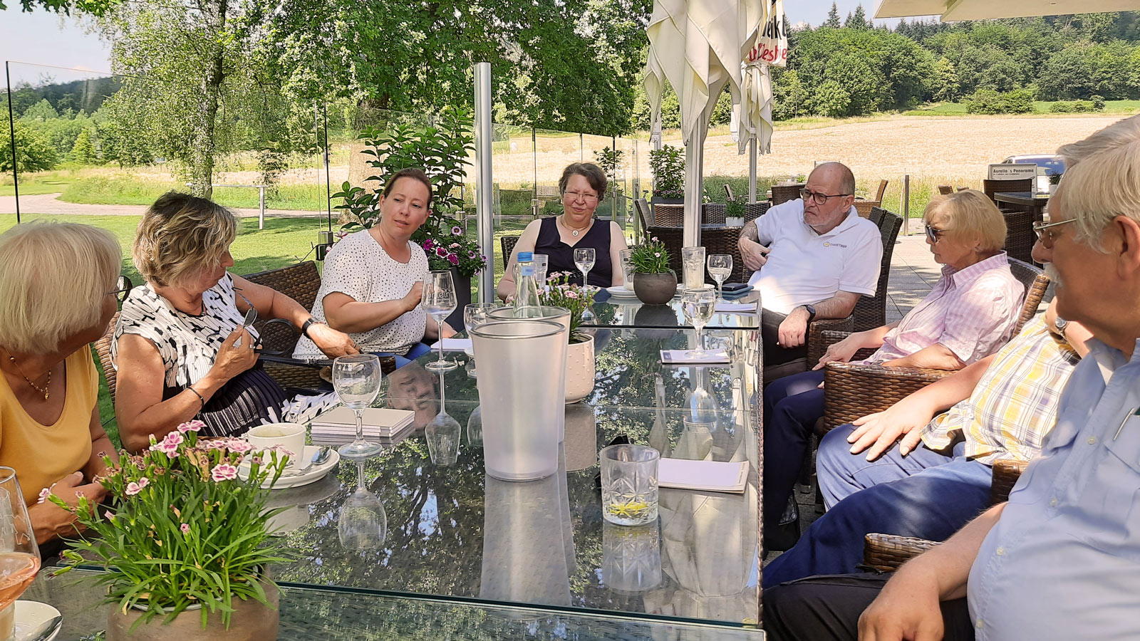 Eine Gruppe Menschen sitzt an einem Tisch auf einer Terrasse bei sonnigem Wetter