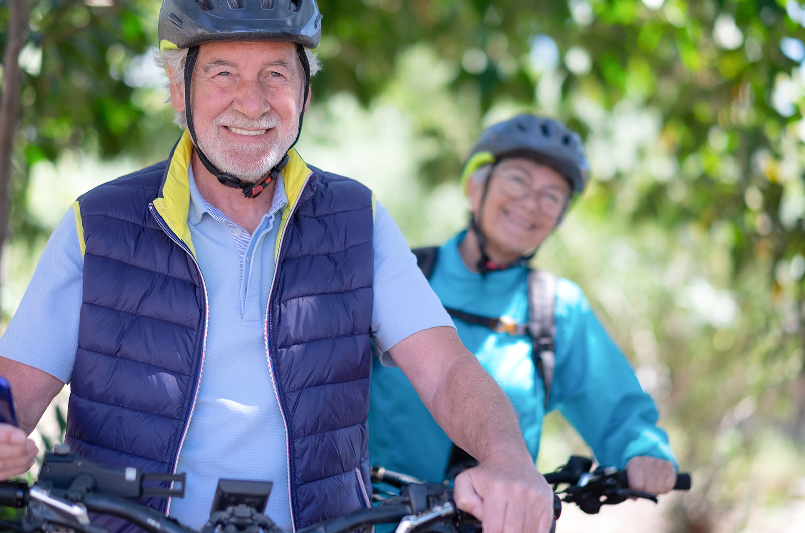 aktives Seniorenpaar mit Fahrradhelm unterwegs in der Natur mit ihren Fahrrädern