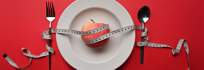 abnehmen und gesundes Ernährungskonzept, ein Apfel auf dem Teller, ein Maßband umschlingt Löffel und Gabel 