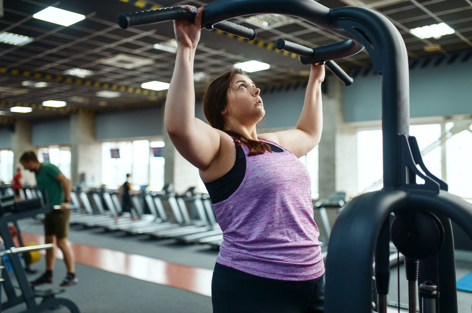übergewichtige Frau am Trainingsgerät, beim Kraftraining im Fitnessstudio