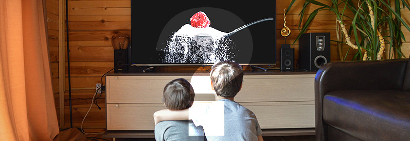 Zwei Jungs sitzen vor dem Fernseher, in dem ein Löffel Zucker zu sehen ist, davor ein Fragezeichen