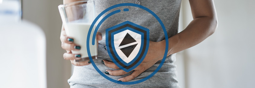 Ein Frau mit einem Glas Milch hält sich den Bauch, davor ein Schutzschild