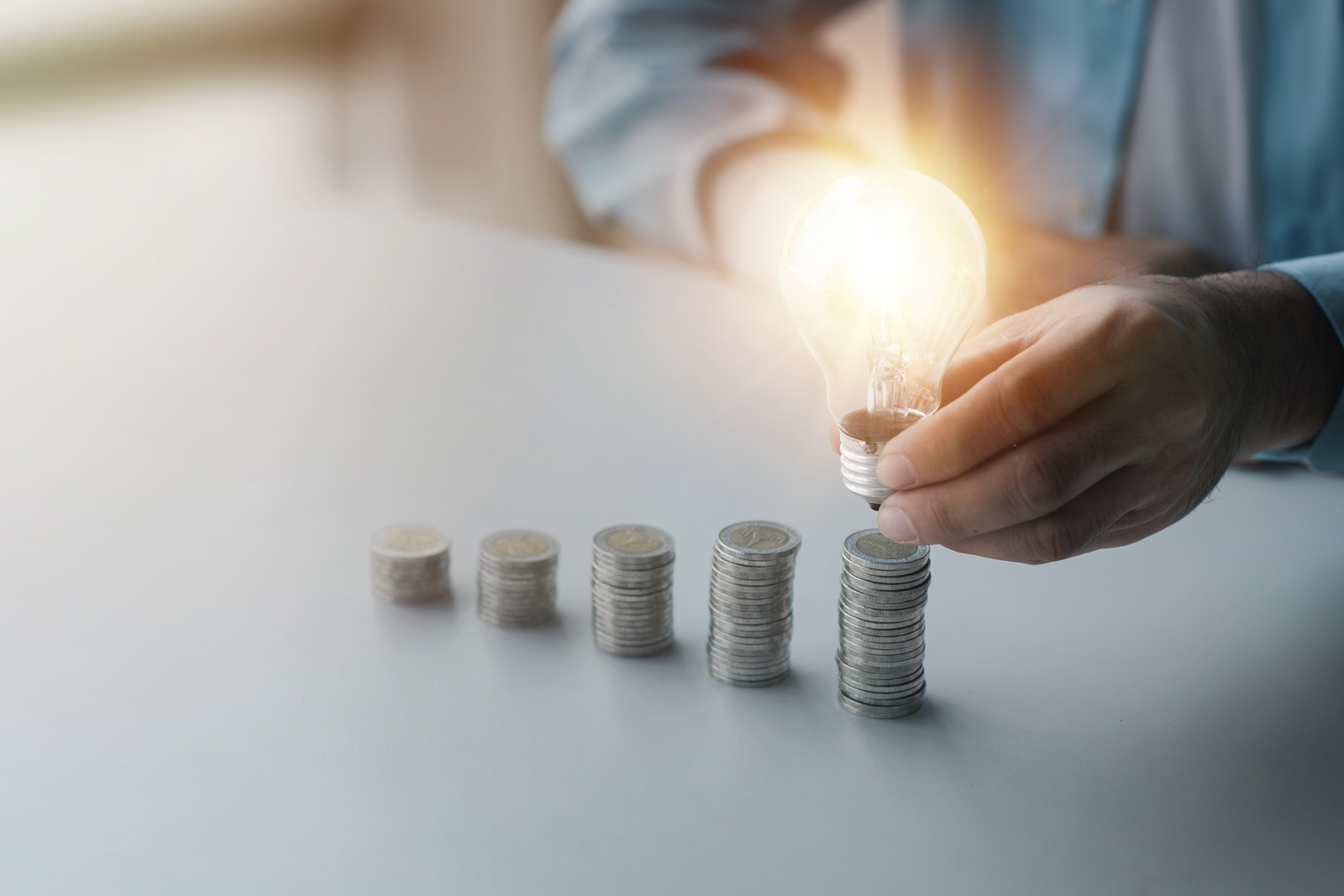 Finanzielle Zuschläge für Expertise Eine Reihung immer größerer werdender Münzstapel. Auf dem höchsten erlechtet eine Glühbirne