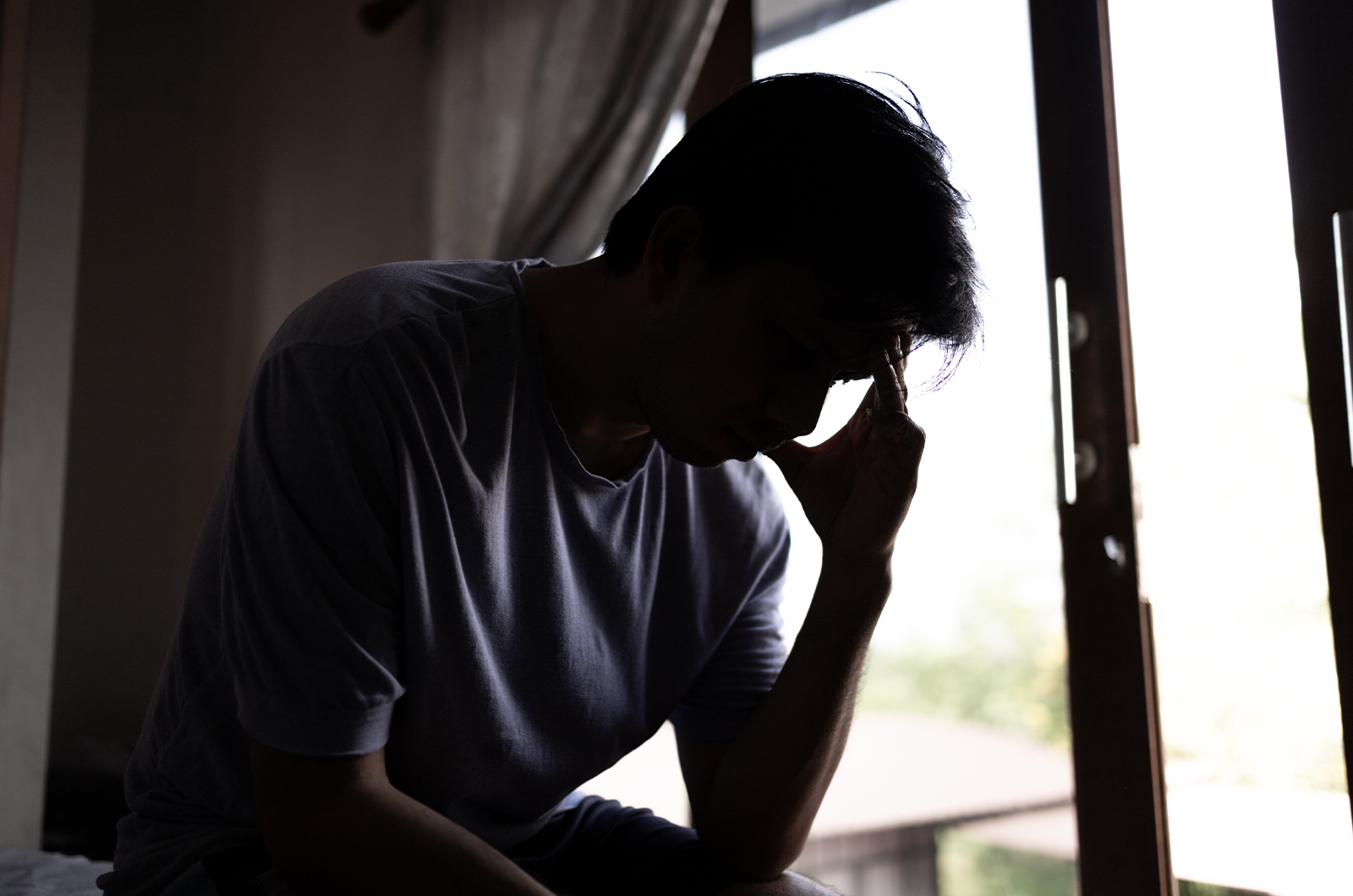 Mann mit psychischer Belastung sitzt in einem Zimmer am Fenster