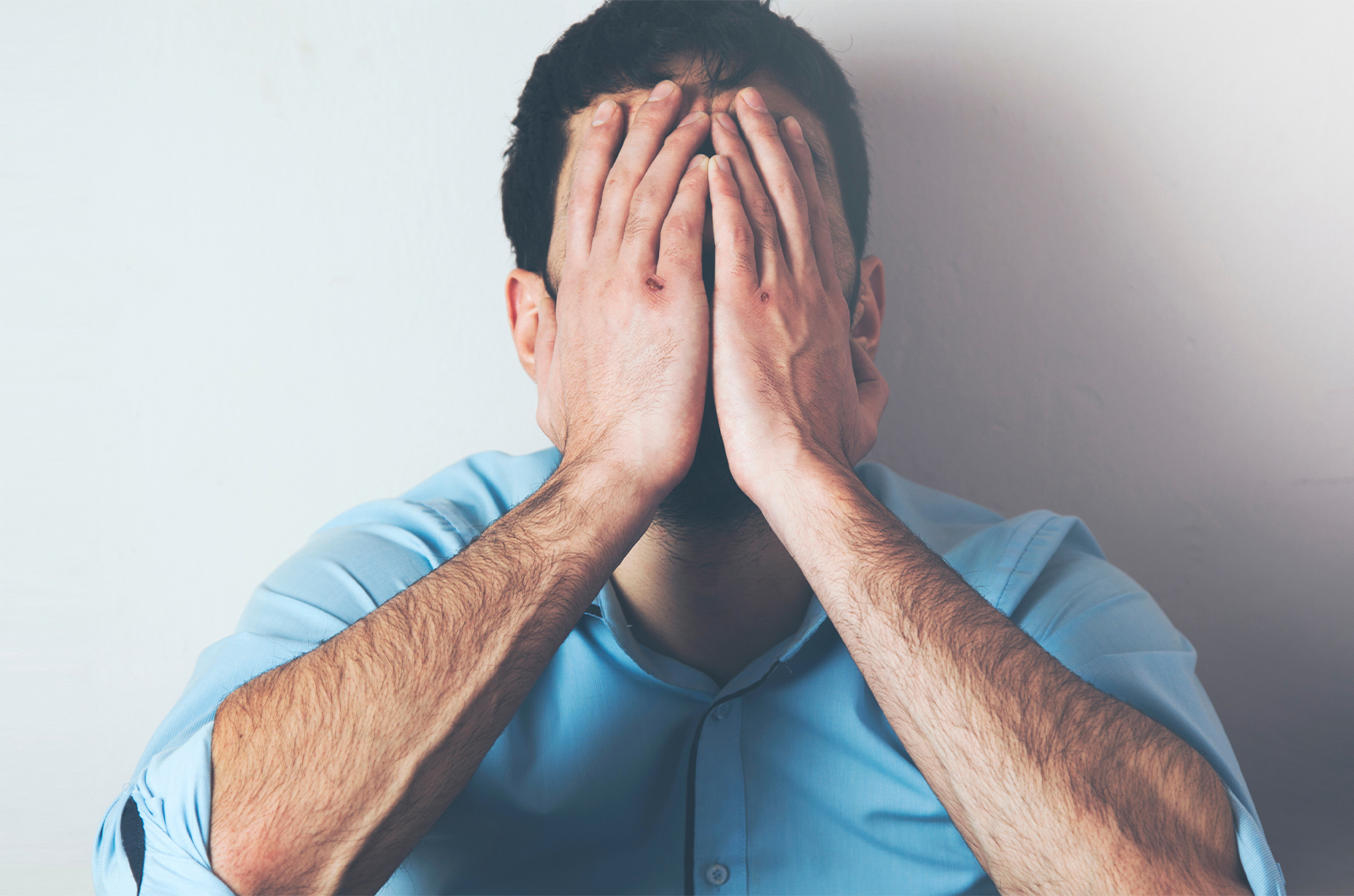 Mann mit emotionaler oder depressiver Belastung, hält seine Hände vor das Gesicht
