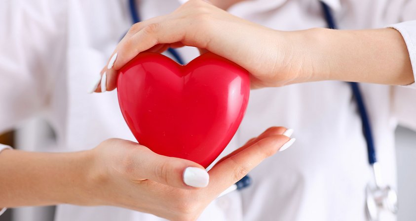 Ärztin schützt mit beiden Händen symbolisch ein rotes Kunststoffherz