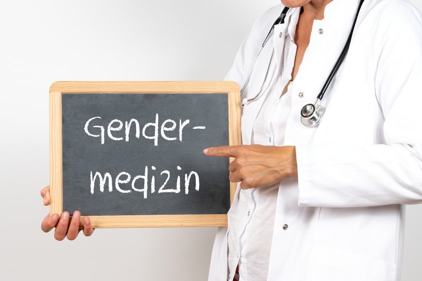 Ärztin mit einer Tafel auf der Gendermedizin steht